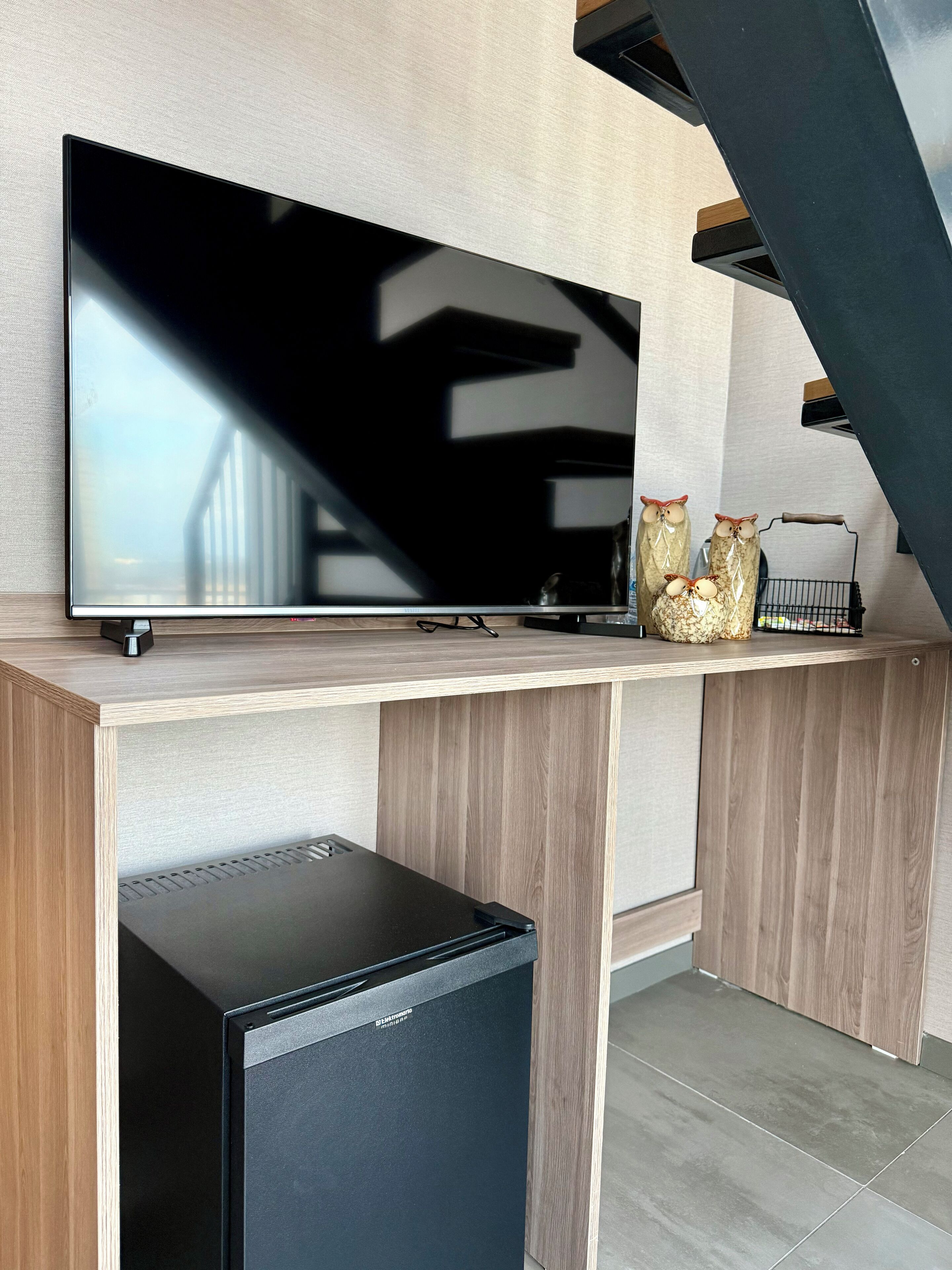 A modern kitchen with a flat-screen TV mounted on a wooden cabinet, a small black refrigerator, and decorative owl figurines on the countertop.