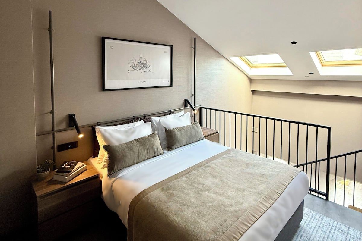 Ein modernes Schlafzimmer mit einem großen Bett, einem Nachttisch, einem gerahmten Bild und Dachfenstern.