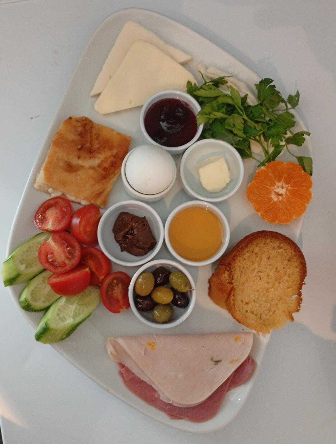 Une assiette contenant divers aliments, notamment du fromage, du pain, des tomates, des concombres, des olives et une tranche d’orange.