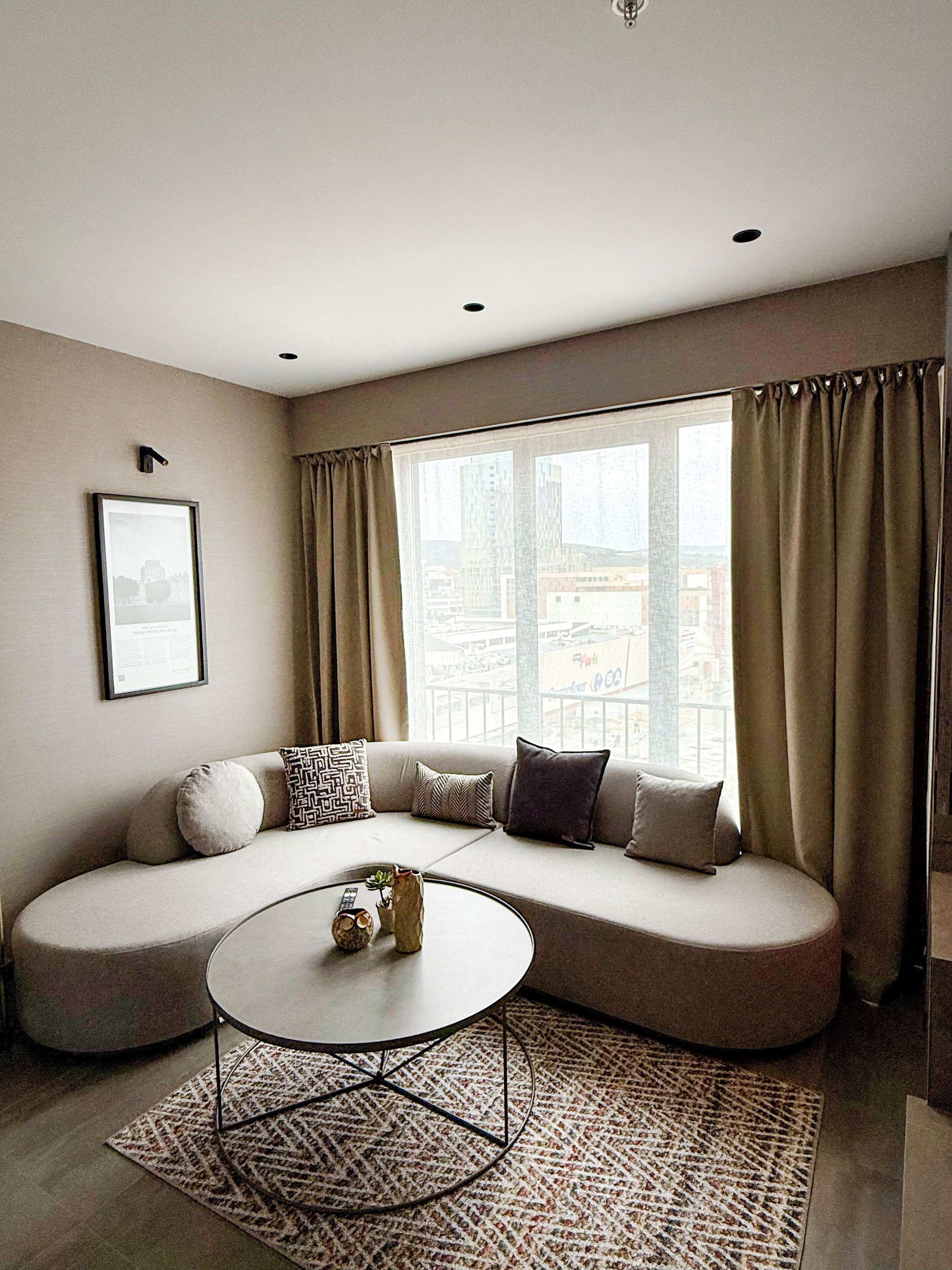 A modern living room with a curved sofa, a round coffee table, and a large window with curtains.
