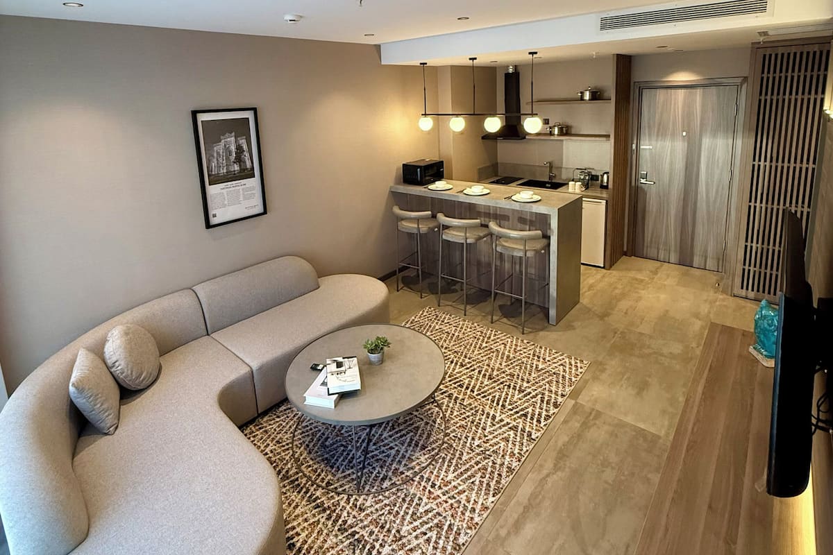 Ein modernes Wohnzimmer mit einer gebogenen Couch, einem runden Couchtisch und einer Küchenzeile mit Barbereich.