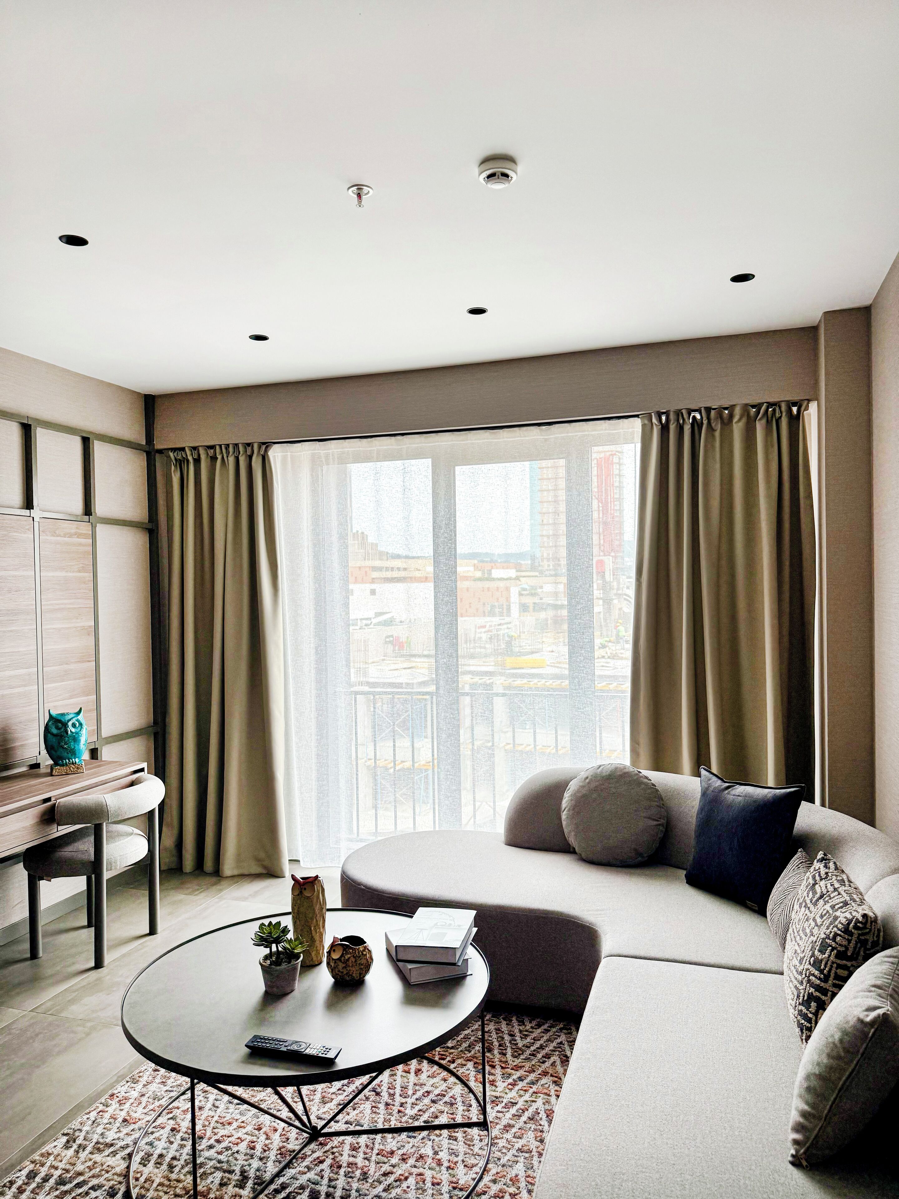 A modern living room with a sofa, a coffee table, and a view of the city through large windows.