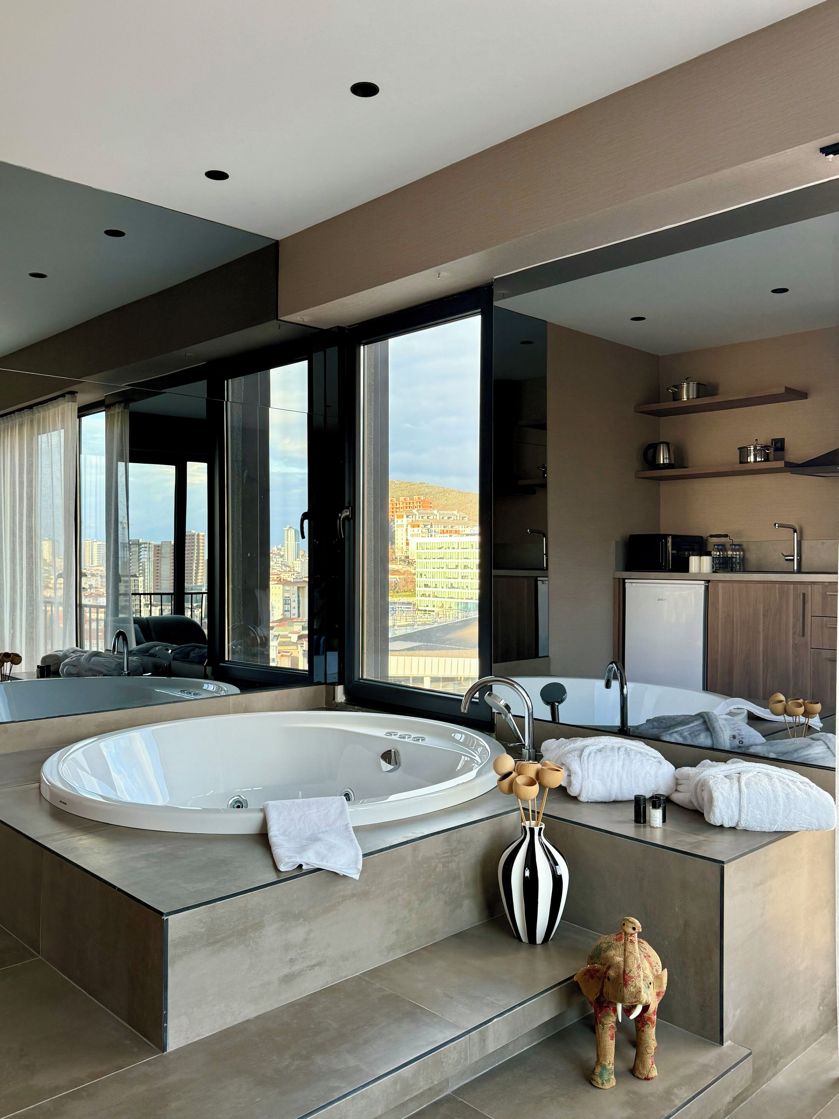 Une salle de bain moderne avec une grande baignoire, un miroir et une vue sur la ville.