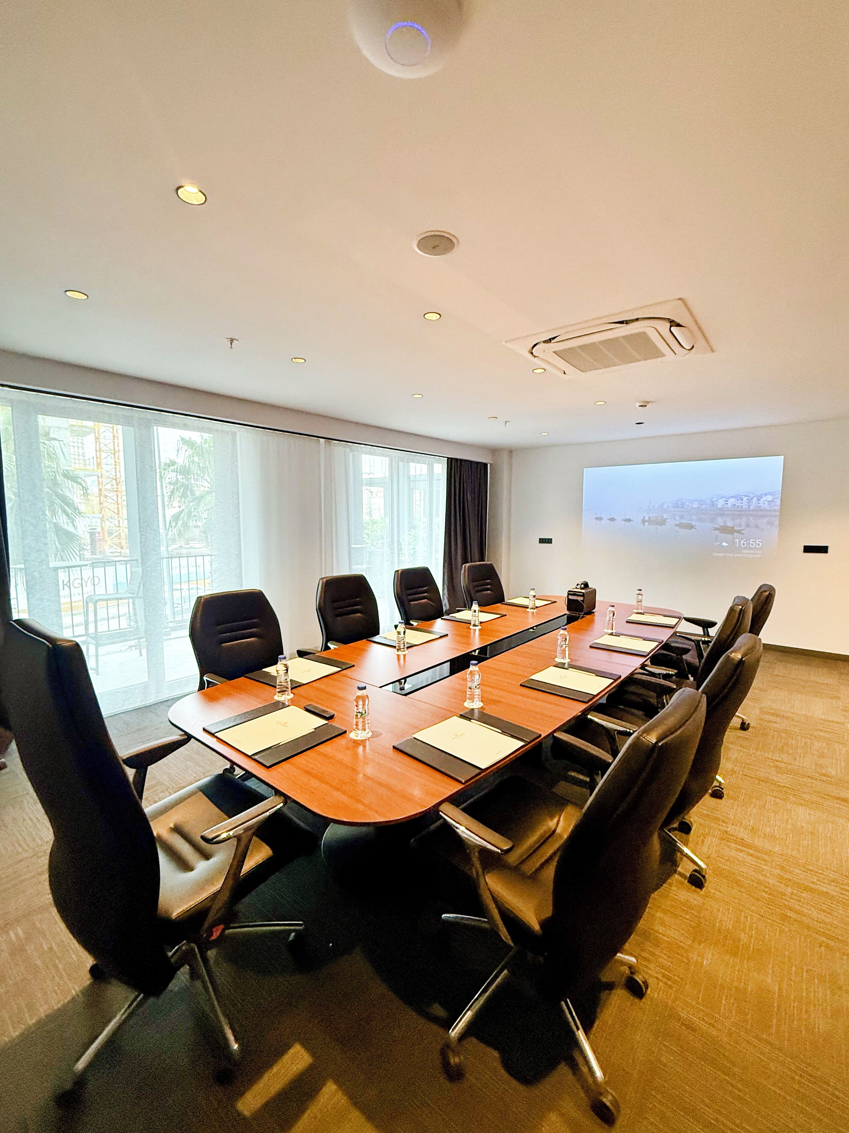 A conference room with a long table, black chairs, and a projector screen displaying a cityscape.