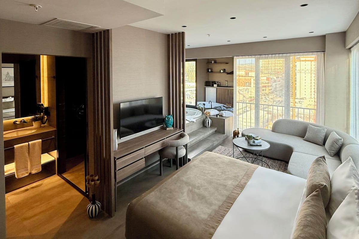 Ein modernes Hotelzimmer mit einem großen Bett, einem Fernseher, einem Schreibtisch und einem Balkon mit Blick auf die Stadt.