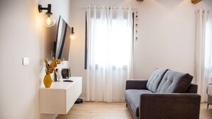 Ein modernes Wohnzimmer mit einem grauen Sofa, einem weißen Konsolentisch mit Vase und Bilderrahmen sowie einem großen Fenster mit transparenten Vorhängen.