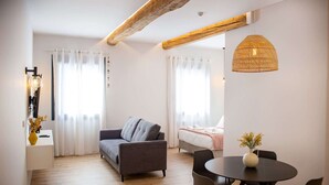 Ein moderner, gut beleuchteter Raum mit einer Couch, einem Bett, einem Esstisch mit Stühlen und einer Pendelleuchte.