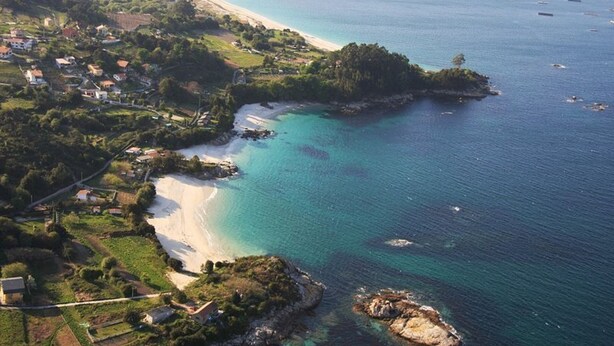 Luftaufnahme einer Küstenlandschaft mit Strand, klarem türkisblauem Wasser und verstreuten Häusern.