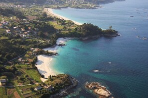 Luftaufnahme einer Küstenlandschaft mit Strand, klarem türkisblauem Wasser und verstreuten Häusern.