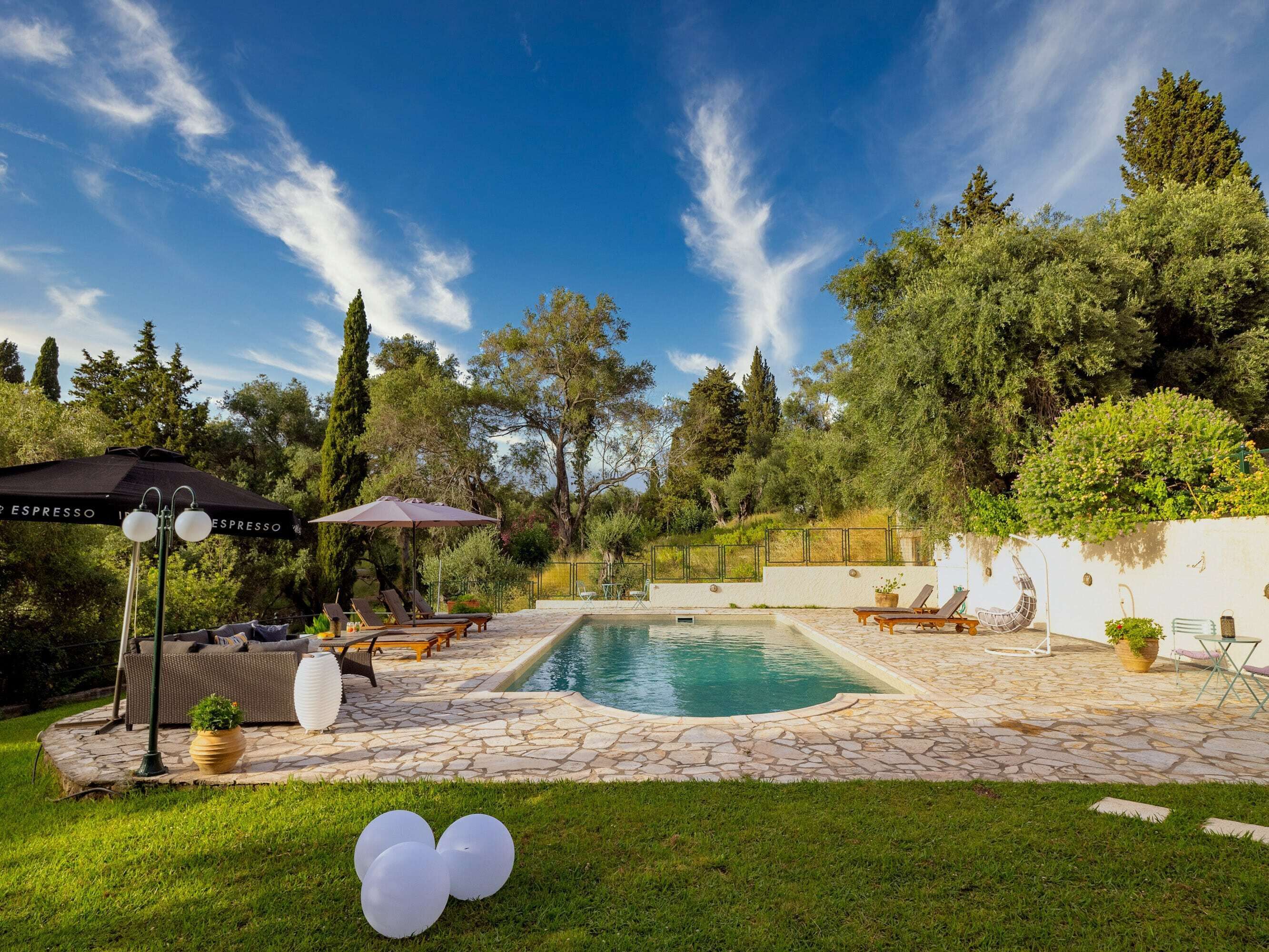 A backyard with a swimming pool, lounge chairs, and a pergola with umbrellas.