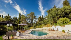 Un jardin avec une piscine, des chaises longues et une pergola ombragée par des parasols.