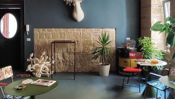 Une pièce avec un mur en pierre, un lustre, un miroir rond et une table avec des chaises.
