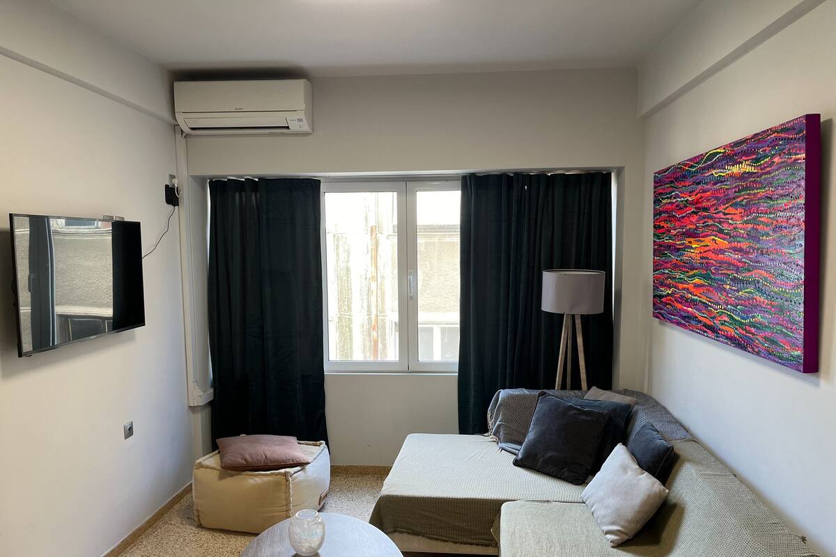 Un salon moderne avec un téléviseur à écran plat, un canapé, une table basse, une lampe sur pied et un grand tableau abstrait.