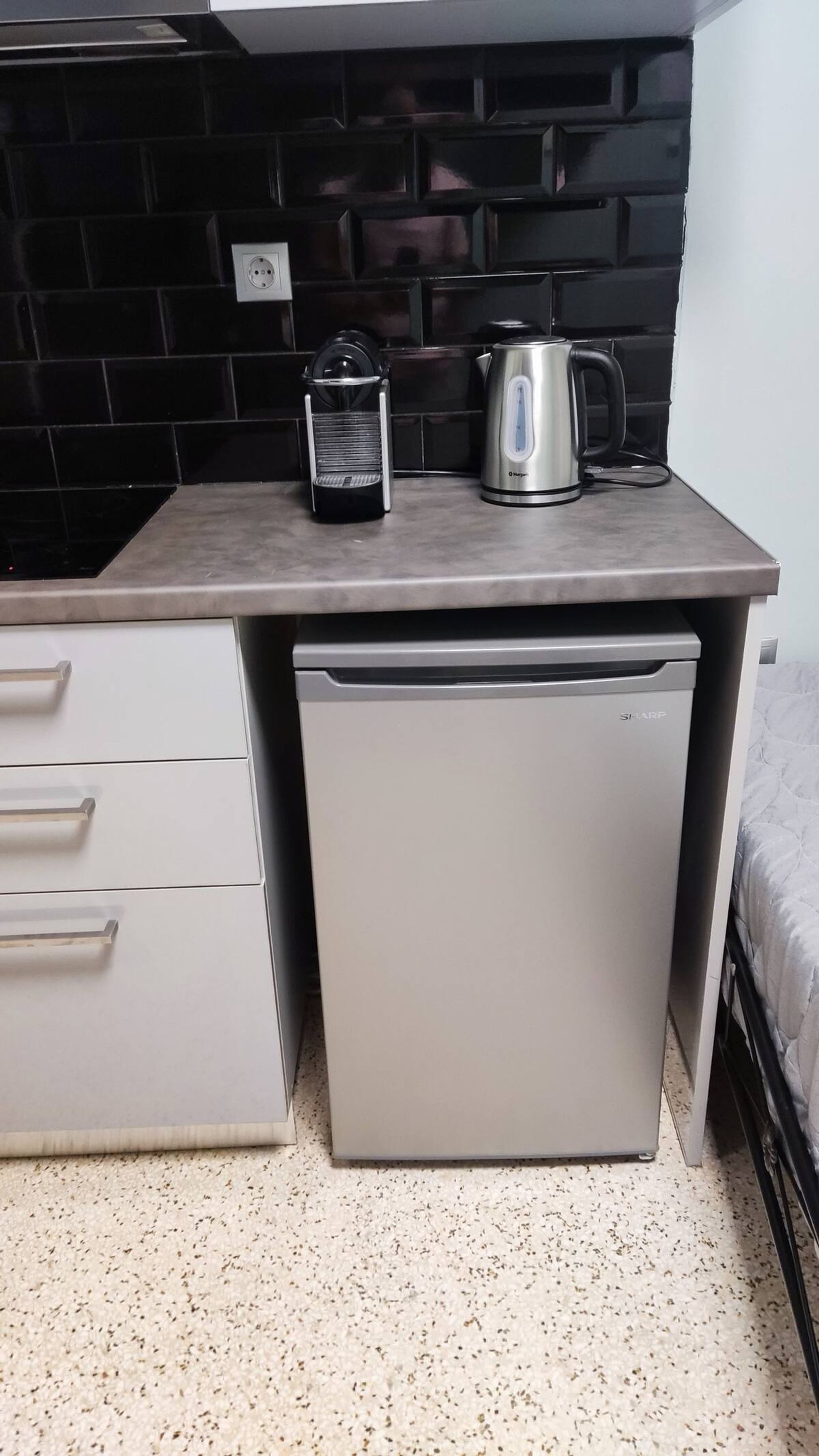 Una kitchenette compacta con una encimera, una cafetera y un refrigerador pequeño.