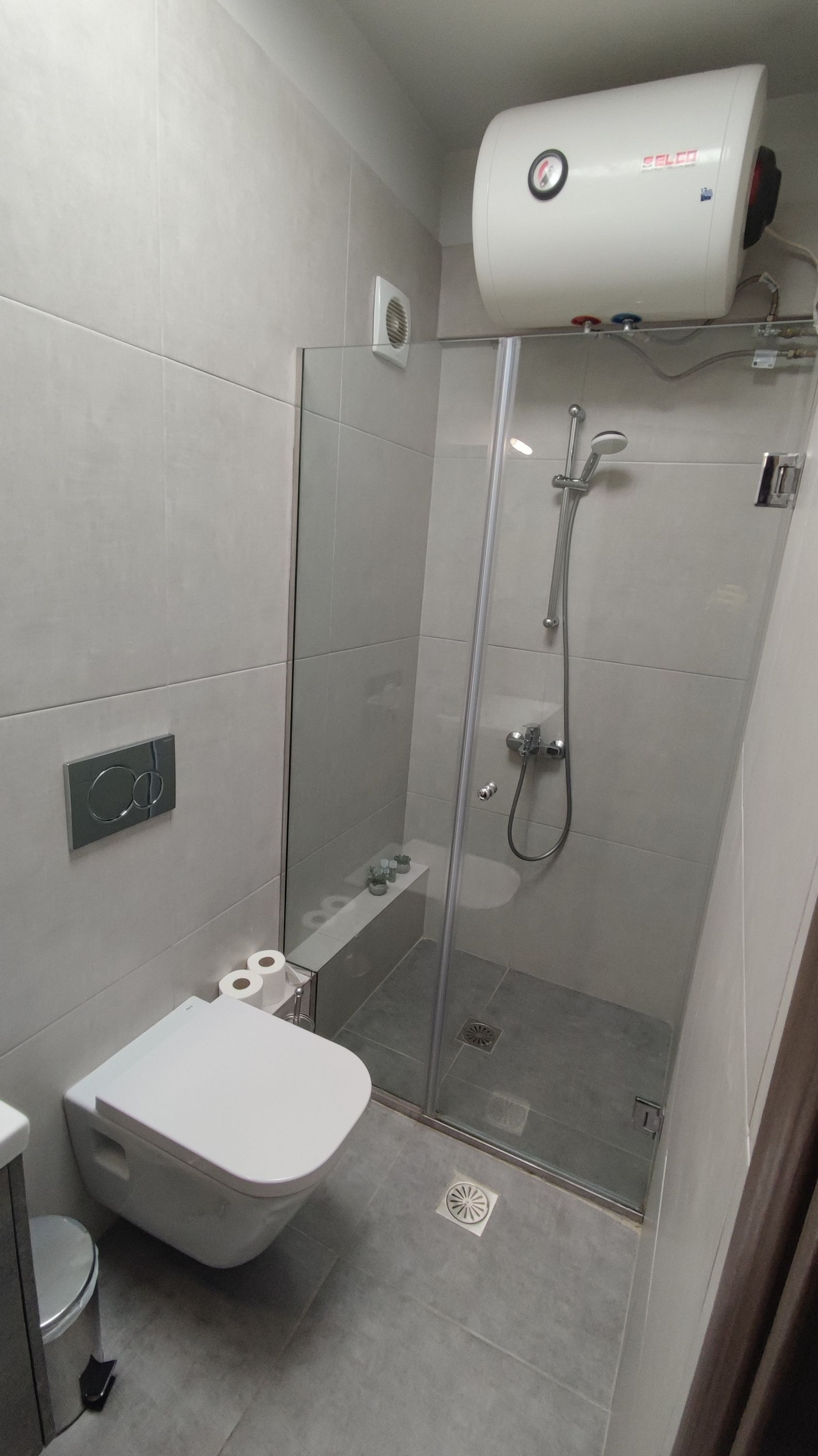 Ein modernes Badezimmer mit einer gläsernen Duschkabine, einer Toilette und einem an der Wand befestigten Föhn.
