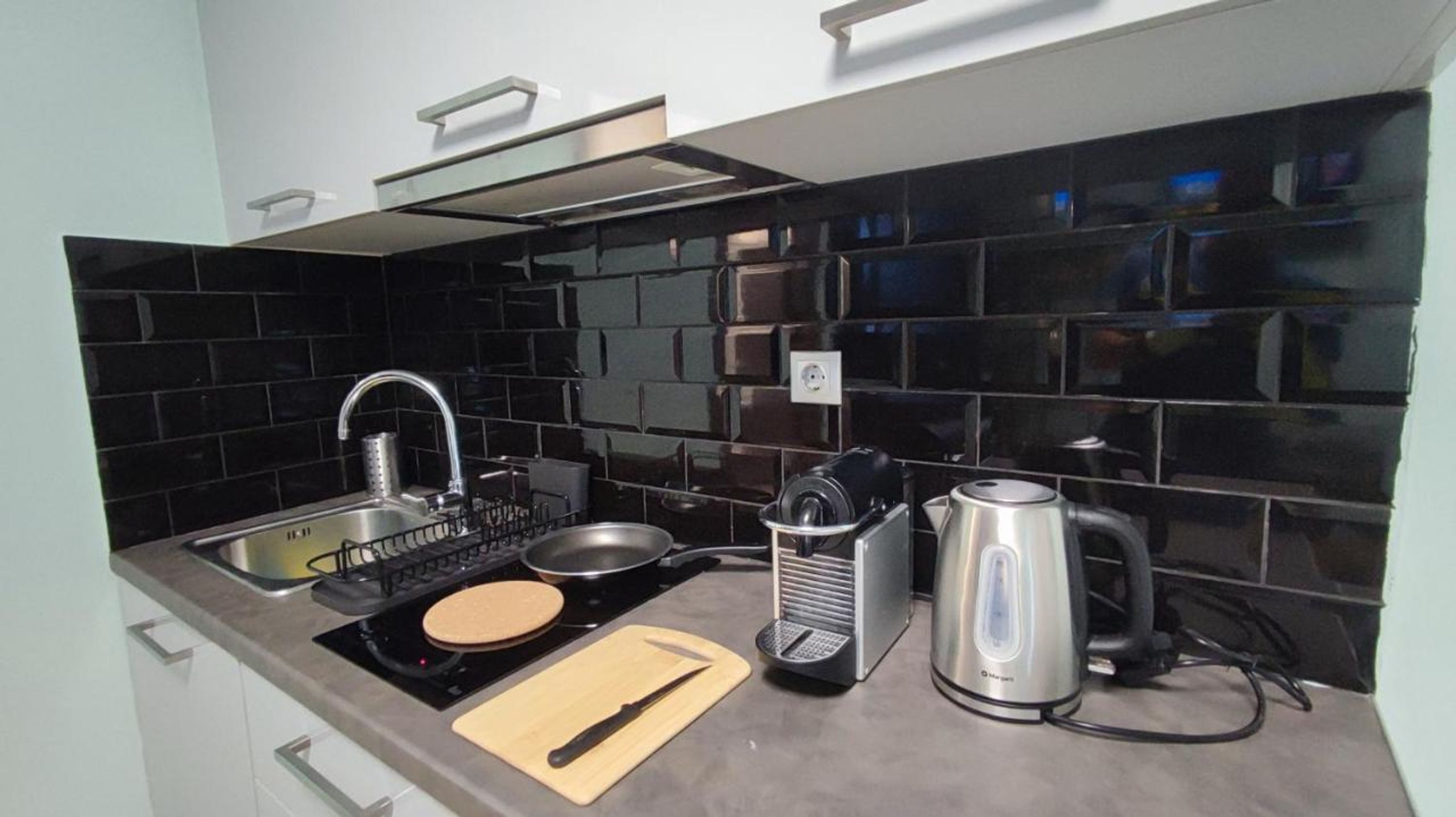 A modern kitchen with black tiles, stainless steel appliances, and a wooden cutting board.