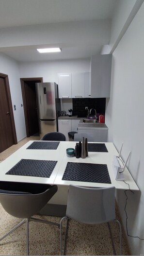 Cozinha compacta com armários brancos, geladeira de aço inoxidável e pia.