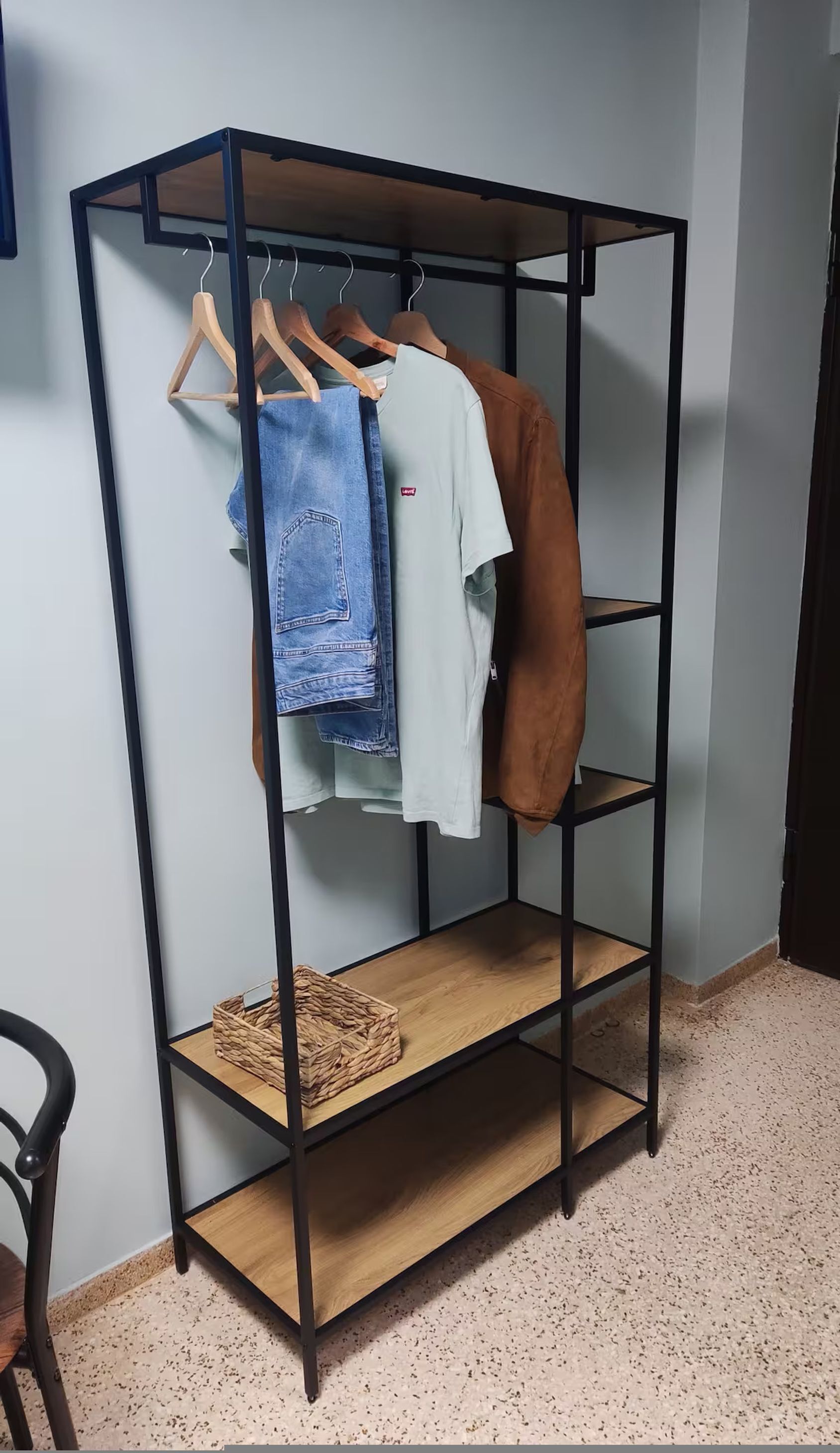 A black metal wardrobe with three shelves, one of which has a woven basket.