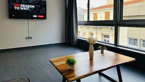 Ein modernes Zimmer mit großem Fenster, einem Holztisch mit Pflanzen und einem Fernseher, der eine Streaming-Dienstanwendung anzeigt.