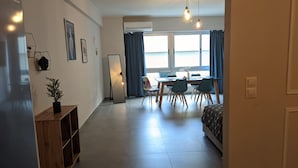 Ein modernes Wohnzimmer mit Essbereich, einem großen Fenster mit Vorhängen, einem Stehspiegel und einer Holzkabine.