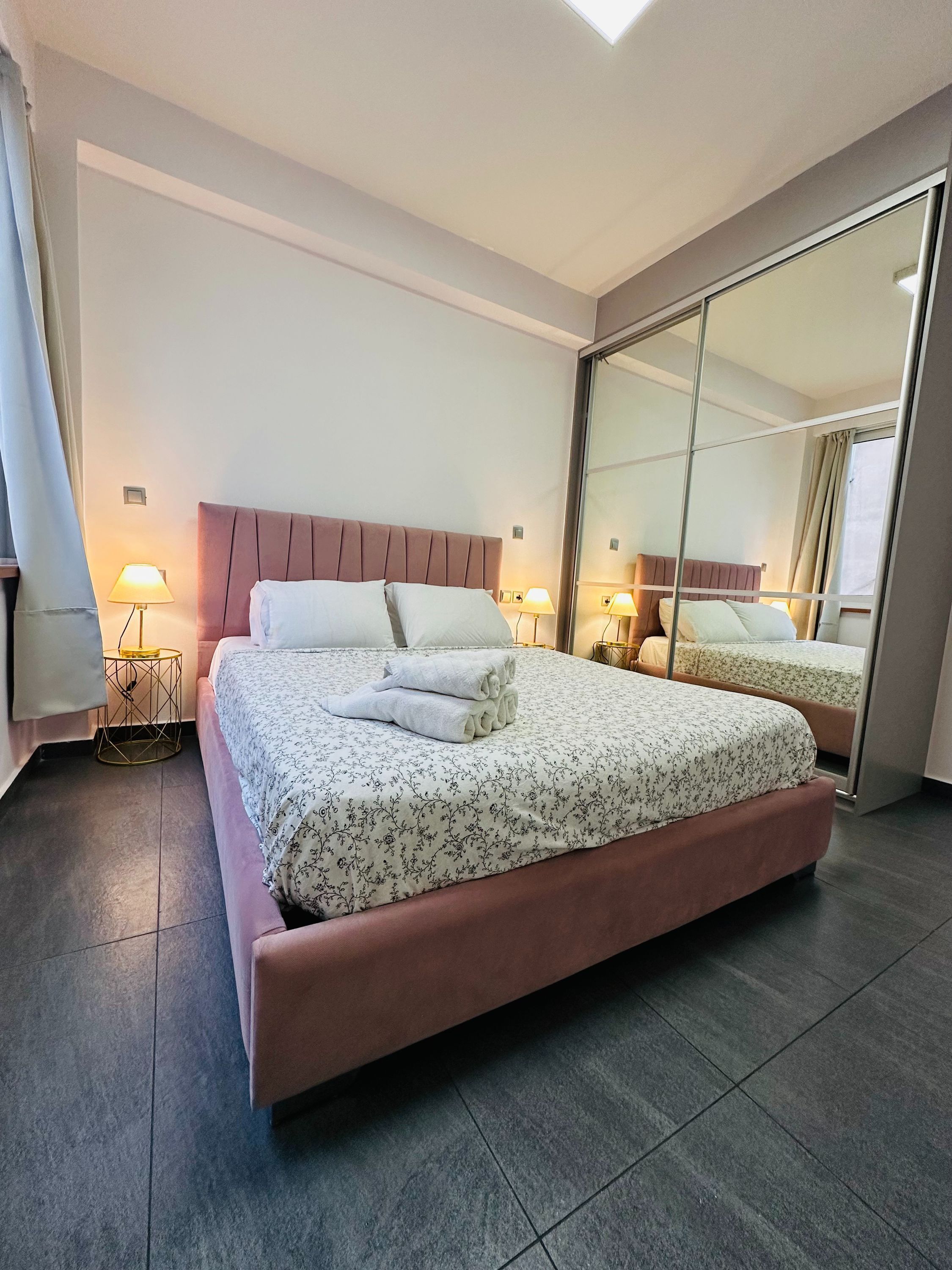 A modern hotel room with a large bed, a mirror, and a small side table.