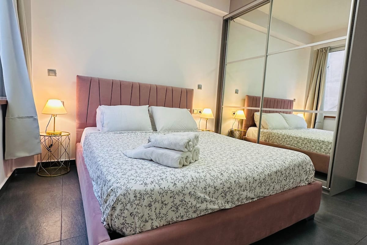 A modern hotel room with a large bed, a mirror, and a small side table.