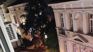 Ein Nachtbild von einem Innenhof mit Steingebäuden, einem Baum und einer Person, die dort entlanggeht.