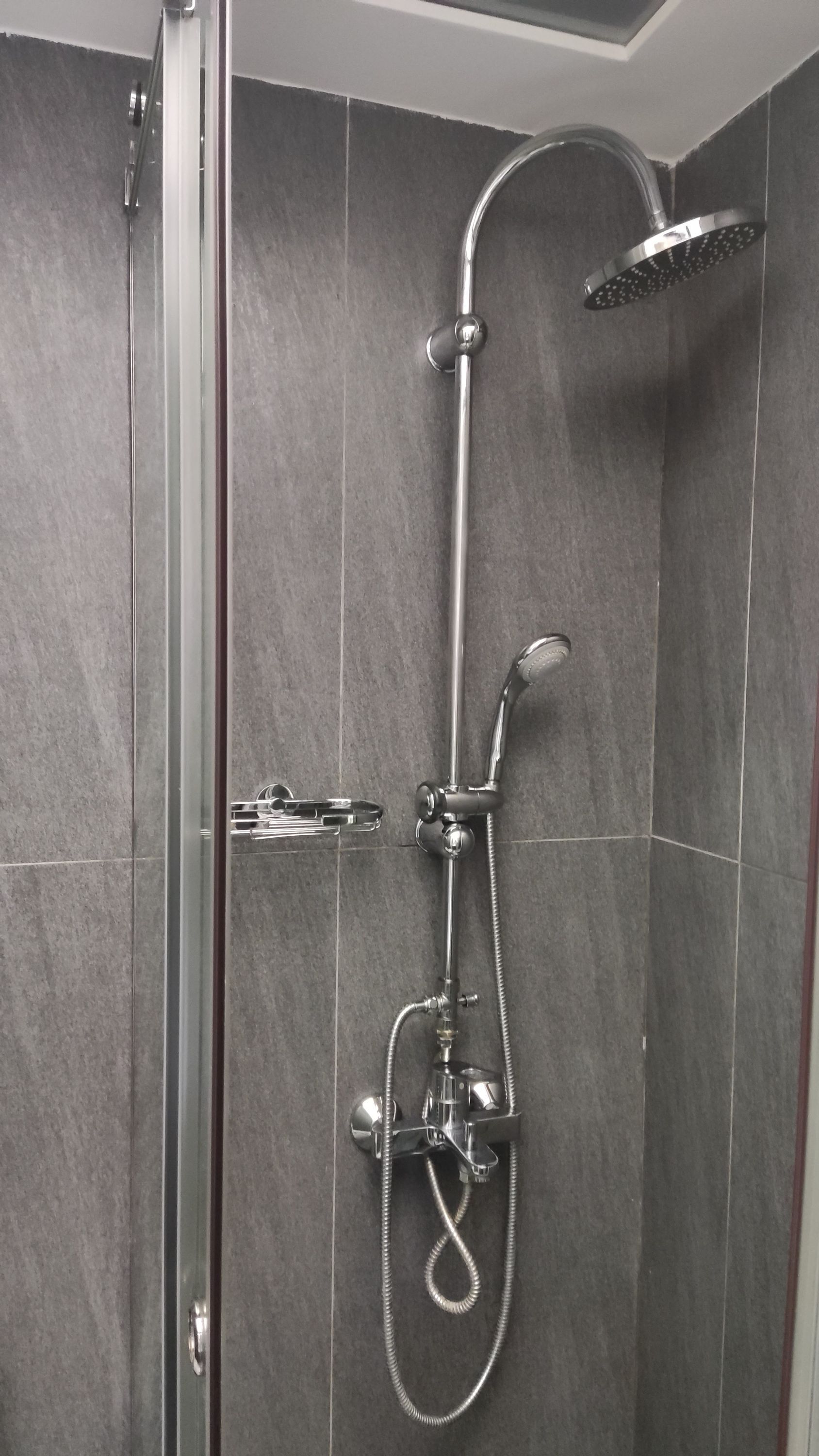A modern shower with a handheld showerhead, a fixed showerhead, and a handheld rain shower attachment.
