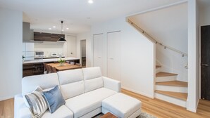A modern living room with a white sofa, a dining area, and a staircase. - MOVA Villa Ozu (Ozu)