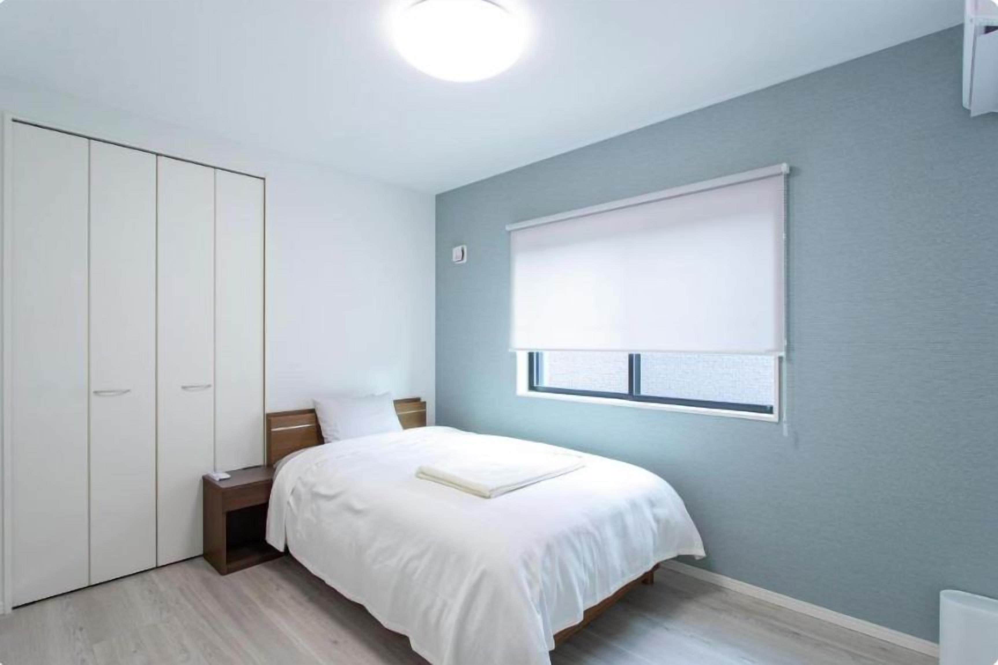 Une chambre à coucher comprenant un lit, une table de chevet, une armoire et une fenêtre avec des stores.