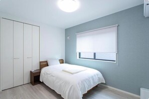 A bedroom with a bed, nightstand, wardrobe, and a window with blinds. - MOVA Villa Ozu (Ozu)
