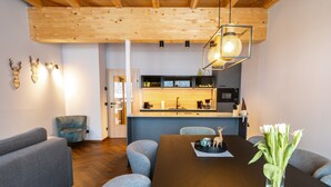 A modern interior with a wooden ceiling, a dining area with a dark wooden table, grey upholstered chairs, a kitchen with a wooden countertop, and a vase of white flowers on the table.