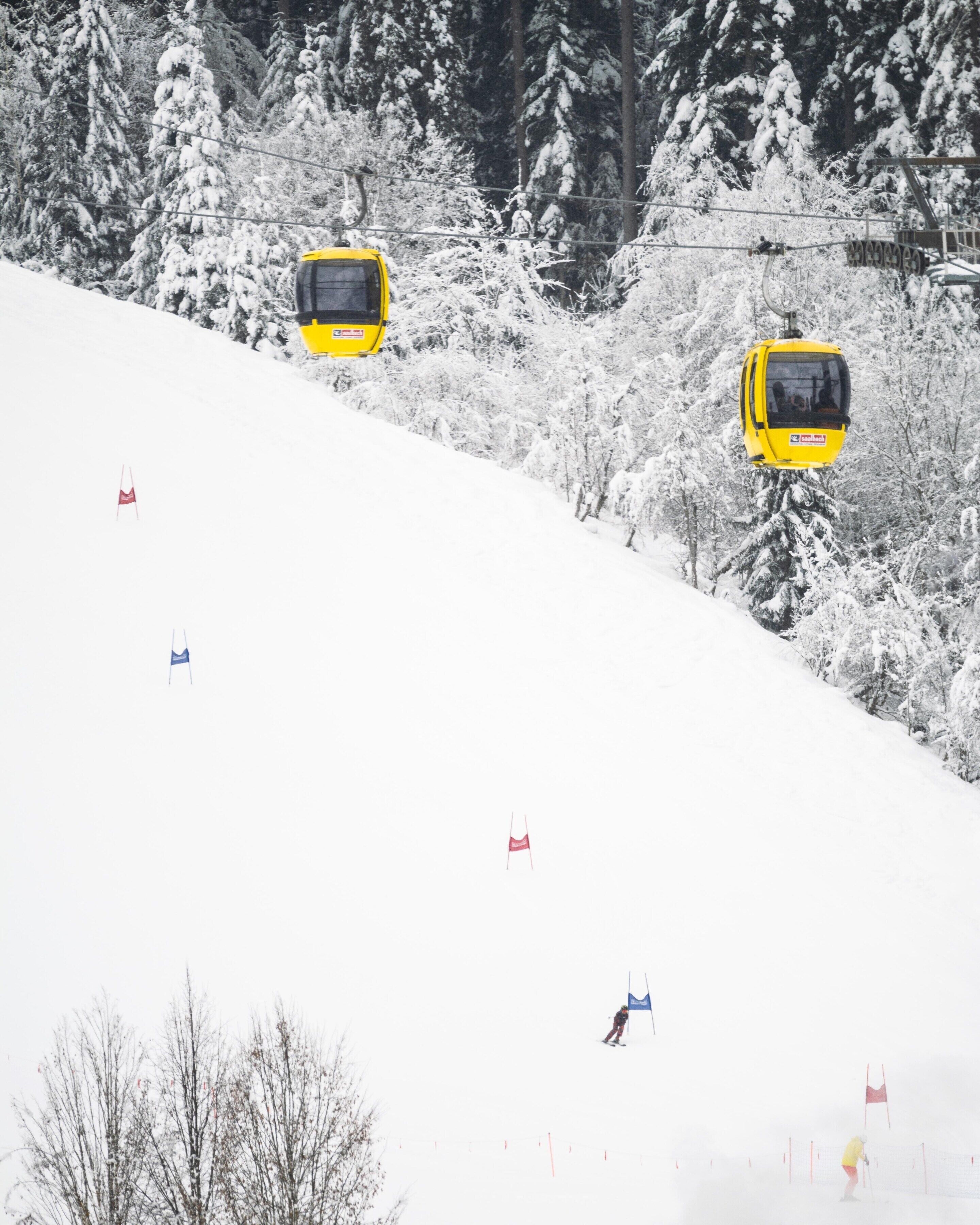 Una pista da sci innevata con una funivia gialla e uno sciatore.