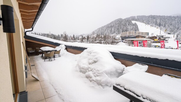 A balcony with a view of a snow-covered landscape, including a ski resort and buildings.