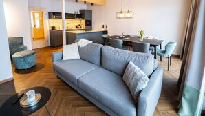 A modern living room with a grey sofa, a dining table, and a kitchen in the background.