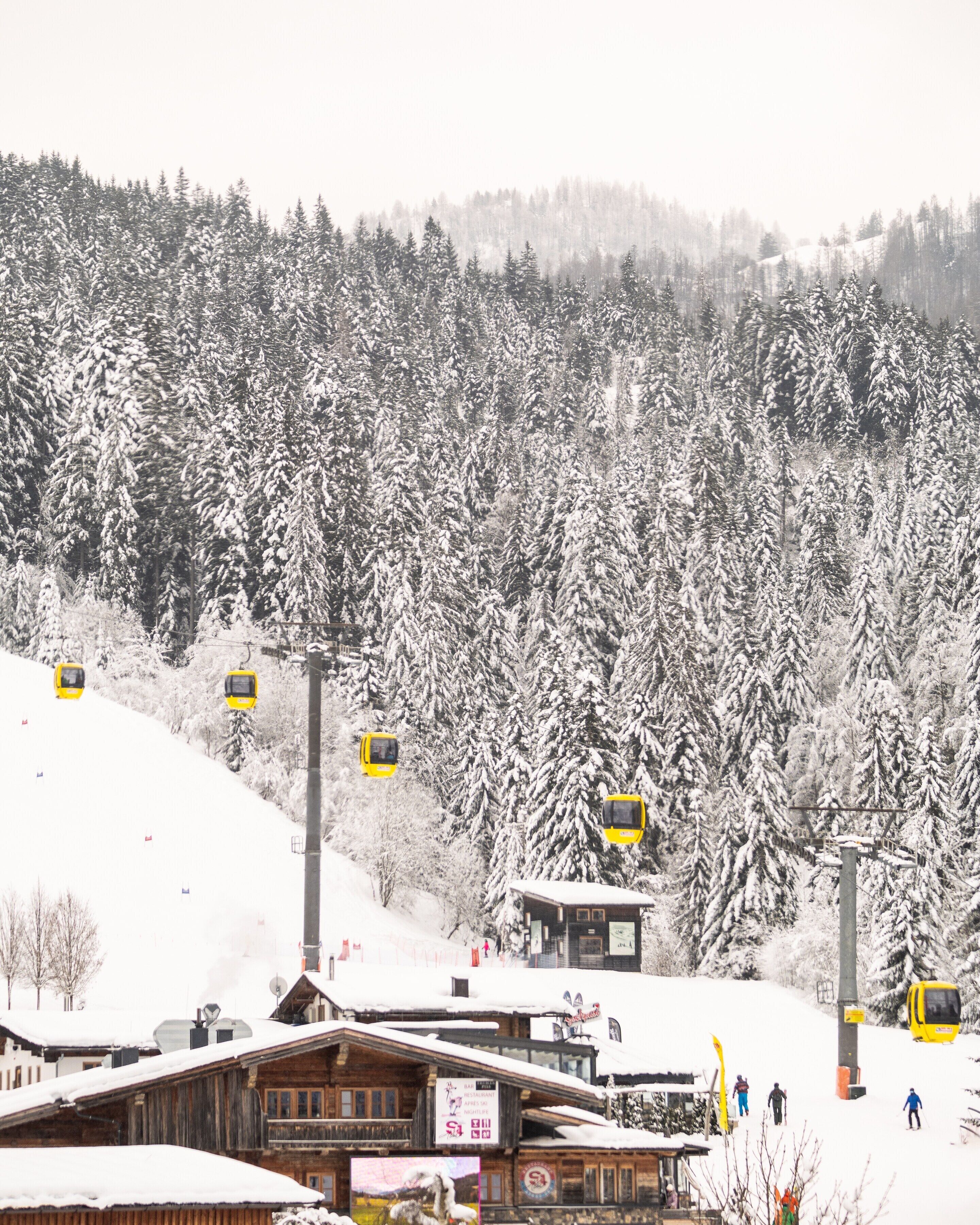 A wooden building with a signboard, surrounded by snow-covered trees and a ski lift in the background.