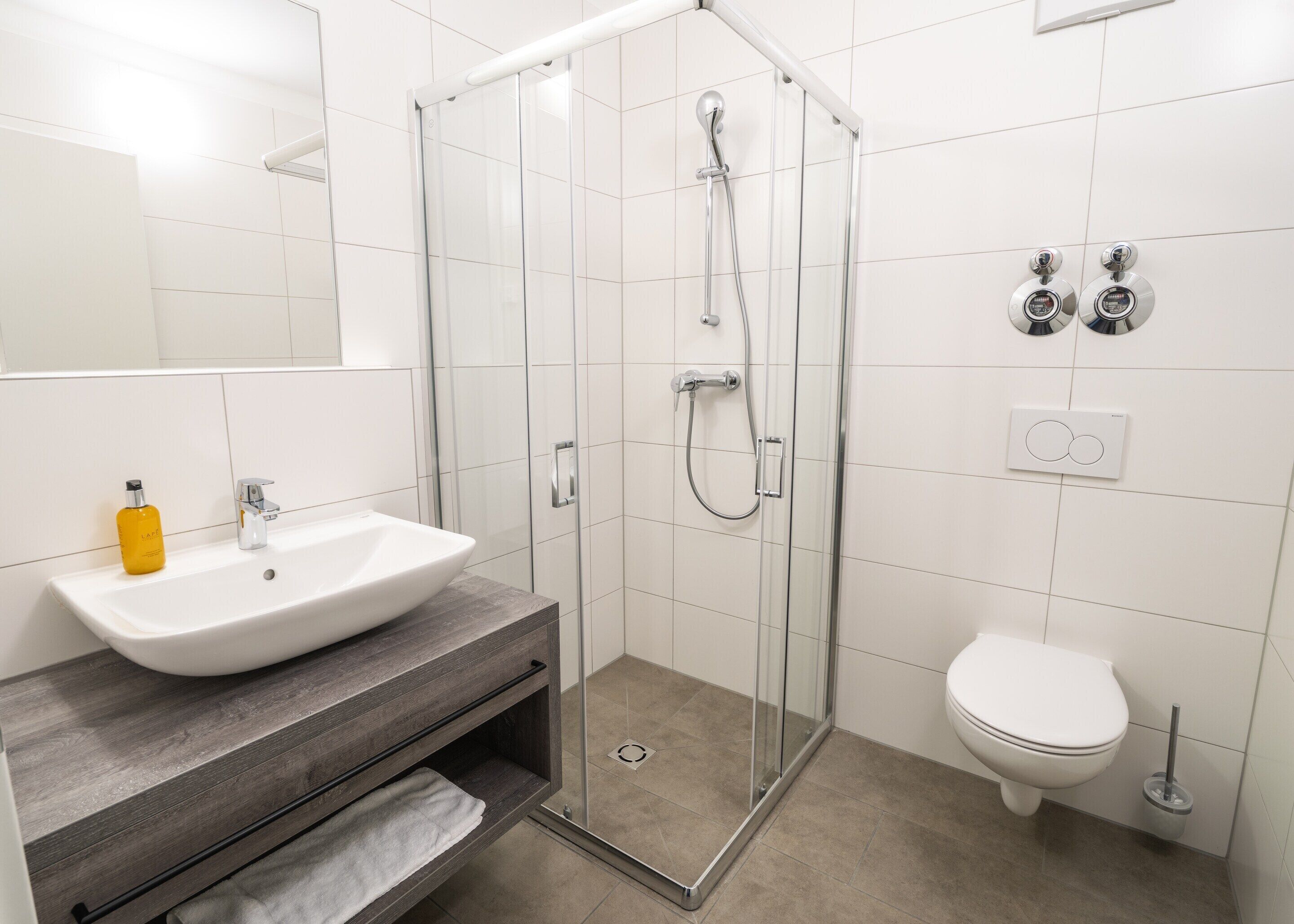 Ein modernes Badezimmer mit einer Duschkabine, einem weißen Waschbecken und einer Toilette.