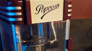 Une machine à pop-corn ancienne, dotée d’une façade en verre transparent, d’une trémie en métal et d’un bouton rouge.