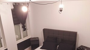 Une chambre à coucher avec un lit, des tables de chevet, une commode, une lampe et une fenêtre avec des rideaux.