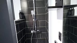 Une salle de bain moderne avec des carreaux noirs, une douche, un lavabo et un miroir.