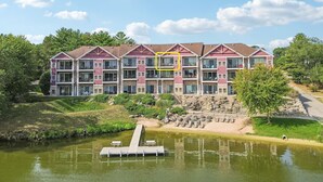 A multi-story hotel with a dock extending into a lake, surrounded by greenery and a clear sky. - Beachtop Condo at Delton Grand - Waterfront (Wisconsin Dells)