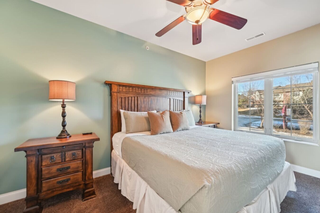 A bedroom with a bed, nightstands, a wooden dresser, a ceiling fan, and a window with a view.