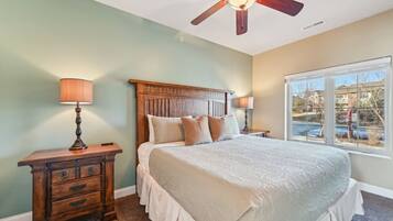 A bedroom with a bed, nightstands, a wooden dresser, a ceiling fan, and a window with a view.