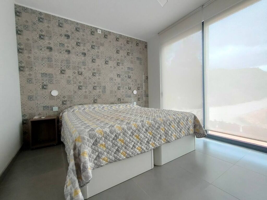 A bedroom with a bed, a nightstand, a patterned wall, and a large window.