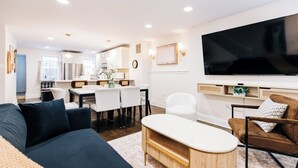 A modern living room with a dark blue sofa, a wooden coffee table, and a large flat-screen TV mounted on the wall.