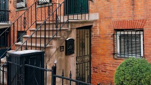 A brick building with a black metal gate, a small potted plant, and a staircase leading to an upper floor.