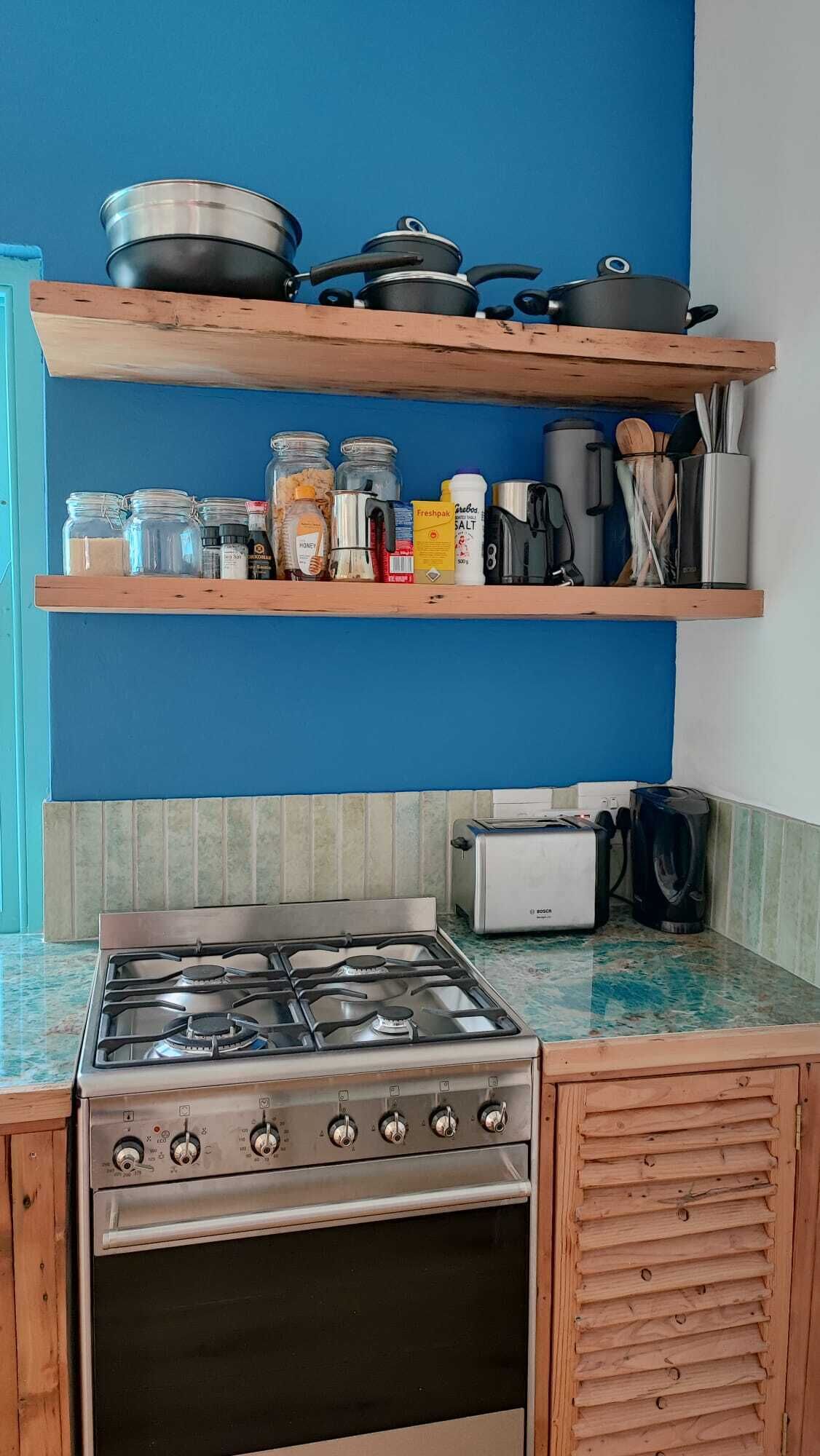 A kitchen with a gas stove, a toaster, and shelves with jars and kitchen utensils.