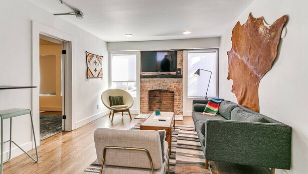 A modern living room with a brick fireplace, a green sofa, and a unique wall art piece.