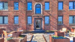 A brick building with a central entrance, outdoor seating, and planters.