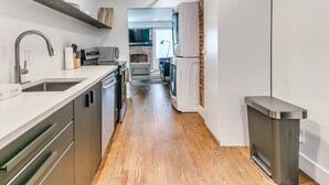 A modern kitchen with stainless steel appliances, wooden flooring, and a brick accent wall.